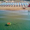 Vista dall'alto di una spiaggia con ombrelloni azzurri e un gonfiabile in mare.