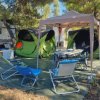 Area campeggio con tende verdi, sedie pieghevoli e tavolo sotto un gazebo.