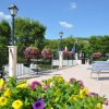 Una terrazza con sdraio blu e bianche, fiori colorati e lampioni, circondata da alberi verdi.