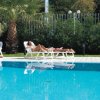 Persone sdraiate su lettini a bordo piscina, tra palme.