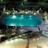 Piscina illuminata di notte con lettini e tavolini intorno.