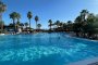 Ampia piscina circondata da palme sotto un cielo azzurro.
