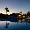 Piscina al tramonto con luci accese e palme riflesse nell'acqua.