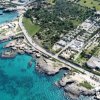 Vista aerea di costa con mare azzurro, verde, edifici e strade.