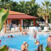 Persone che nuotano sotto una fontana in piscina, con palme e una struttura con tetto rosso.
