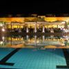 Piscina illuminata di notte con persone cenanti sotto pergole.
