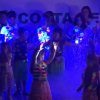 Bambini su un palco sotto luci colorate, indossano abiti festivi.