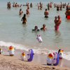 Spiaggia affollata con persone in acqua e giochi a forma di pinguino sulla sabbia.