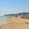 Spiaggia affollata con bagnanti e ombrelloni, colline verdi sullo sfondo.