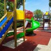 Parco giochi con scivoli colorati e pavimentazione in gomma rossa.