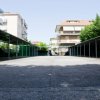 Un parcheggio vuoto con tettoie laterali, circondato da edifici residenziali e alberi.