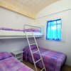 Camera con due letti singoli e un letto a castello, copriletti colorati e finestra blu.