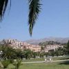 Vista su un paesaggio cittadino con palme, edifici su una collina e montagne sullo sfondo.