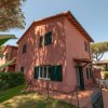 Casa rosa con giardino e alberi intorno.