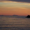 Tramonto sul mare con silhouette di una scogliera.