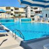 Piscina azzurra con lettini e ombrelloni a strisce blu e bianche, edifici sullo sfondo.