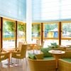 Sala con vetrate, tavolini e sedie in vimini, cuscini verdi. Ambiente luminoso e rilassante.