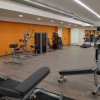 Palestra moderna con attrezzi e pesi su pavimento in legno, pareti arancioni e specchi.