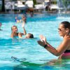 Un'istruttrice in piscina guida una lezione di aquagym; le persone seguono i movimenti.