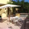 Terrazza con ombrellone e sedie bianche, circondata da muretti e vegetazione.