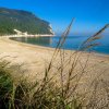 Spiaggia sabbiosa con mare calmo e montagne verdi sullo sfondo.