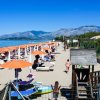 Spiaggia con ombrelloni arancioni, persone su lettini e monti sullo sfondo.