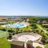 Panorama di un villaggio turistico con piscina, campi da tennis e mare.