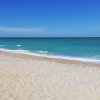 Spiaggia sabbiosa con mare turchese e cielo blu.