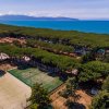 Campo da tennis tra alberi e vista sul mare con montagne lontane.
