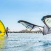 Persone fanno kitesurf in mare, con un molo sullo sfondo.
