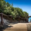 Sentiero in legno tra dune sabbiose conduce al mare, circondato da vegetazione.