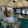 Interno di una veranda con tavolo coperto da tovaglia e sedie in plastica bianca.