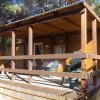 Veranda in legno con sedie e tavolo, circondata da alberi.