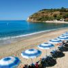 Spiaggia con ombrelloni bianchi e blu vicino al mare limpido.