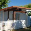 Bungalow bianco e azzurro con tetto rosso-marrone e un piccolo patio, circondato da alberi.