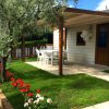 Casetta con veranda, sedie da giardino bianche e prato con fiori rossi.