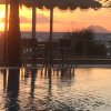 Tramonto sul mare con palme e tavoli in primo piano.