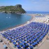 Spiaggia affollata con ombrelloni blu e mare sullo sfondo.