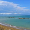 Spiaggia con mare calmo e dighe frangiflutti sotto un cielo coperto.