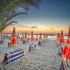 Spiaggia all'alba con ombrelloni a righe arancioni e blu.