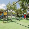 Un parco giochi con scivolo blu e altalene circondato da alberi.