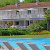 Piscina con sdraio e un edificio a due piani sullo sfondo circondato da giardini.