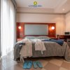 Camera d'albergo con letto matrimoniale, tende bianche, ciabatte azzurre e vestiti sparsi.