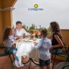 Famiglia di quattro persone seduta a tavola su un balcone con drink e cibo.