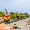 Una donna su una terrazza con un bicchiere di aperitivo. Vista sulla strada e sul mare.