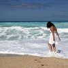 Una persona cammina sulla spiaggia con i piedi nell'acqua, indossa un abito bianco.