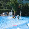 Persone giocano in una piscina poco profonda circondata da lettini e palme.