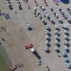 Vista aerea di una spiaggia con file ordinate di ombrelloni bianchi e blu.