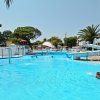 Piscina all'aperto con scivolo e persone che nuotano. Sullo sfondo, palme e una giornata soleggiata.