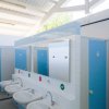 Bagni pubblici con cabine blu e lavandini bianchi sotto uno specchio.